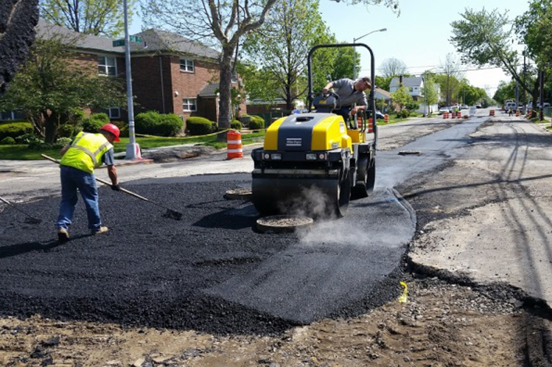 Crews work to spread asphalt on a road.