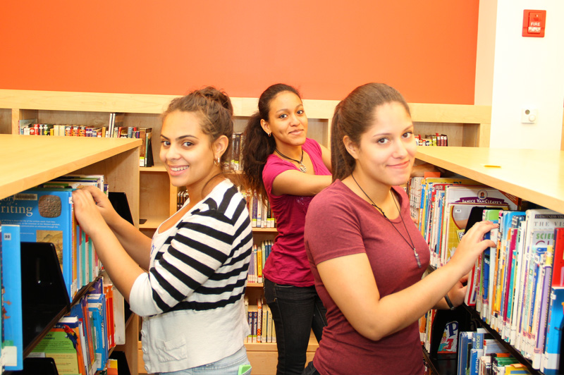 three girls in library posing by books