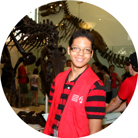 Student posing for picture in front of dinosaur skeletons