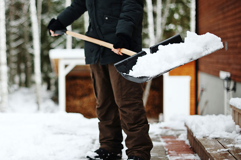A person wearing cold weather gear holding a shovel with snow on it.