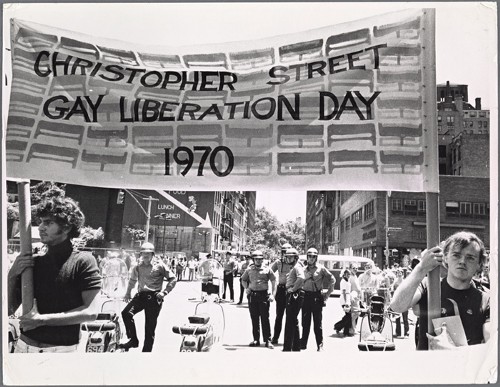 A black and white photo of people marching holding up a banner that states Christopher Street Gay Liberation Day 1970