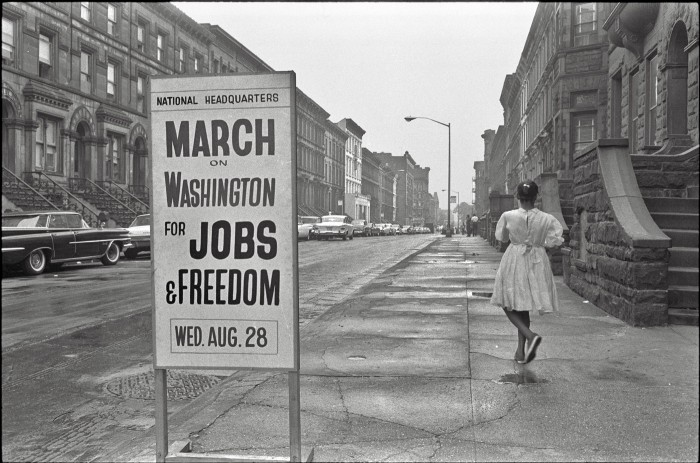 a vintage black and white photo of a view  down a block of house and a sign on the side walk posted National Headquarters March on Washington for Jobs and Freedom Wed August 28