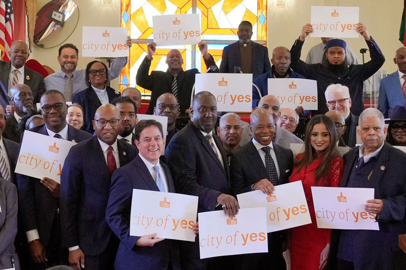 Mayor Adam along a group of faith-based leaders holds a paper with text reads, City of Yes