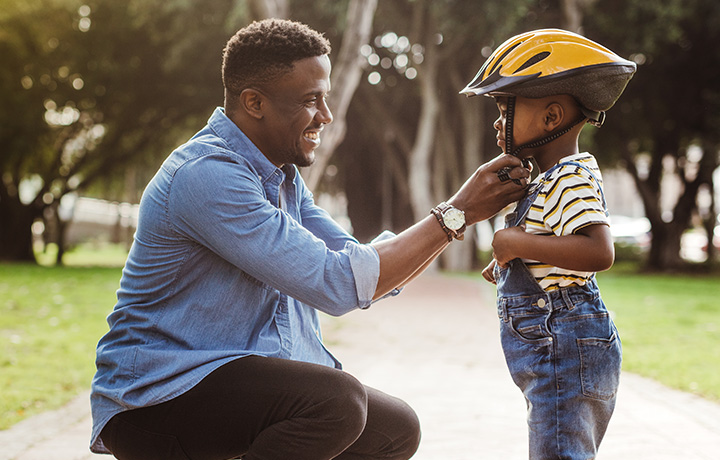 Person smiling while fastening a helmet for a child
                                           