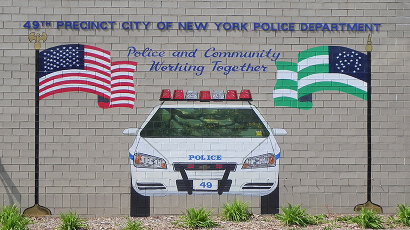 On the external wall of the 49th NYPD Precinct House, a mural shows two flags, a police car, and text that says police and community working together
                                           