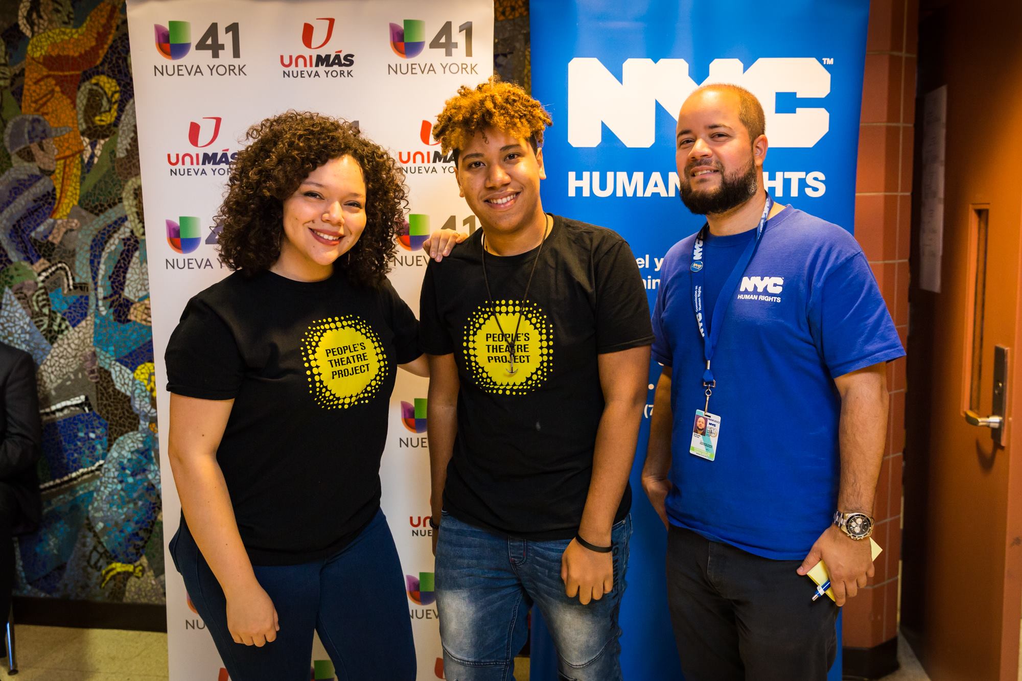 Three people posing for camera; two people are wearing “People’s Theater Project” t-shirts, and one person is wearing “NYC Human Rights” t-shirt.