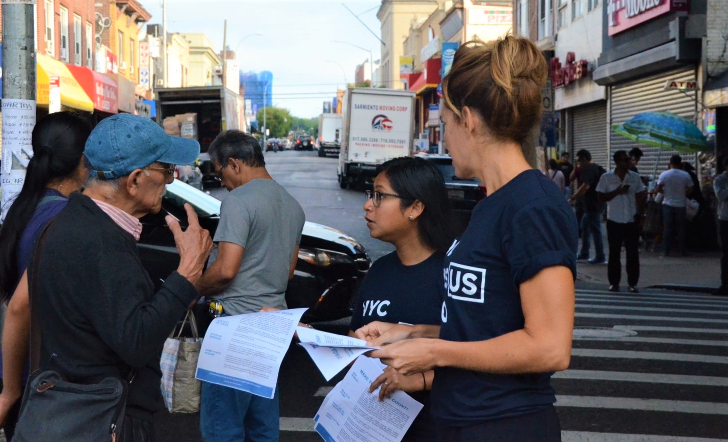 Two people wearing census shirts talking with an older gentleman on a street.