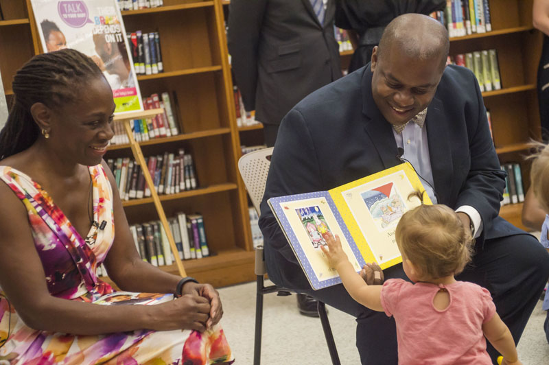 First Lady Chirlane McCray sitting alongside a man reading a book to child