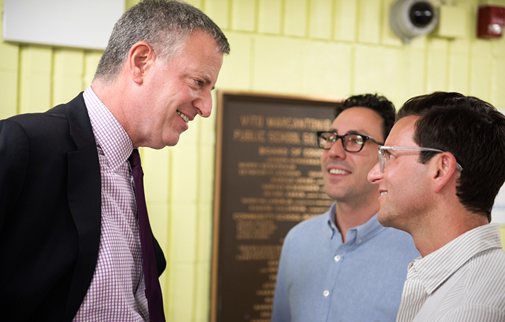 Mayor de Blasio speaks to two males while smiling
                                           