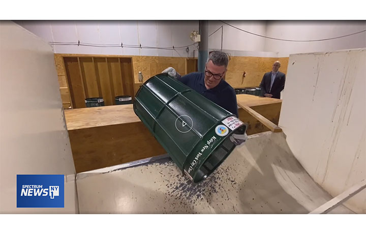 Man lifts metal trash can and dumps contents into a simulated garbage truck
                                           