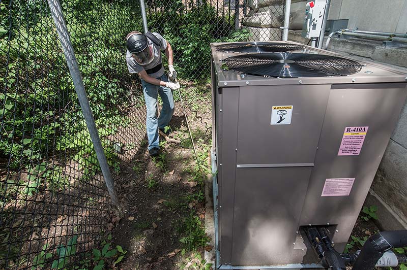 A City staff person wearing a face mask and gloves outside of a facility using a portable coil cleaner to clean condenser coils as part of a preventative maintenance program.