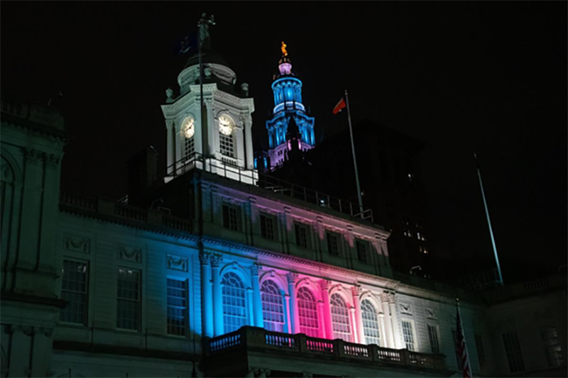 New York’s City Hall illuminated at night with multiple colors
                                           