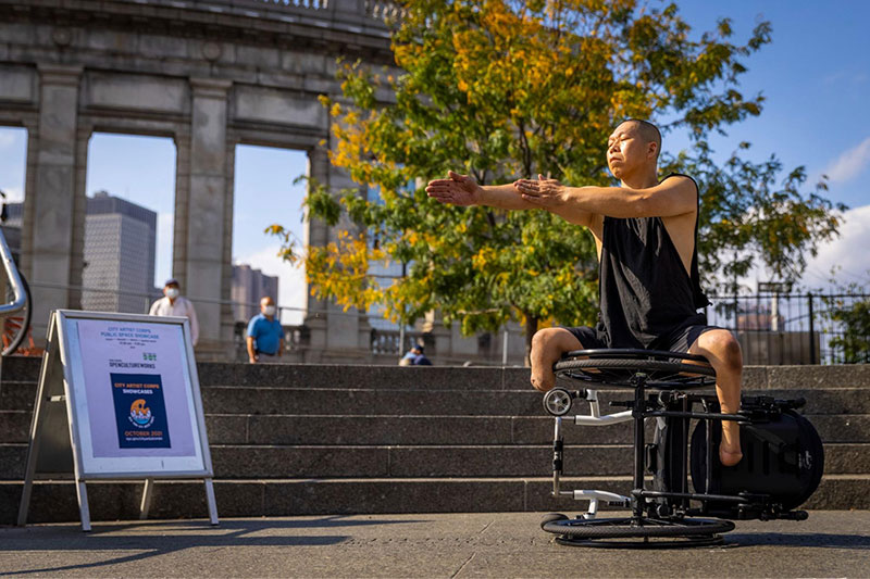 A performer with a disability dances, arms reached out sitting on a wheelchair