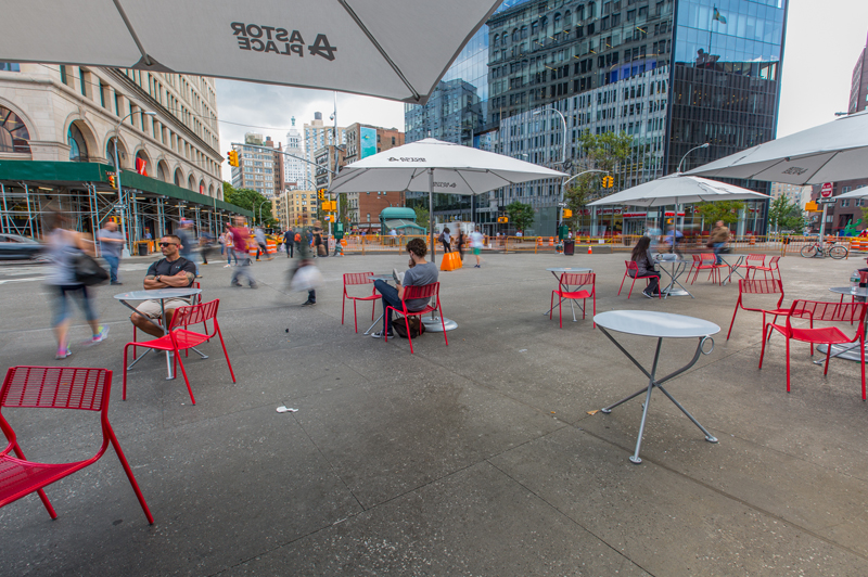People sit in bright red chairs on Alamo Plaza in Astor Place.