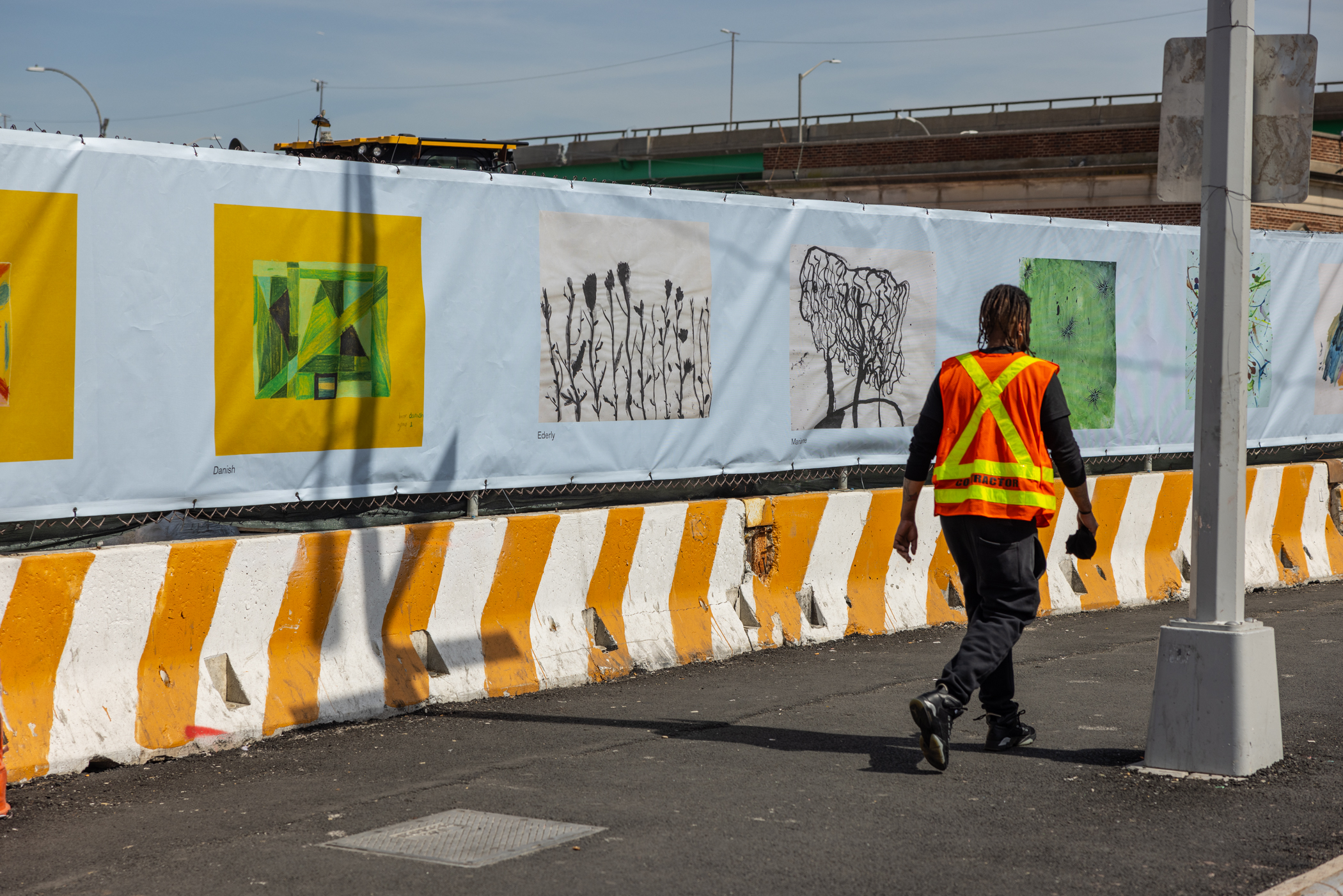 pedestrian walks by fencing with artwork on it