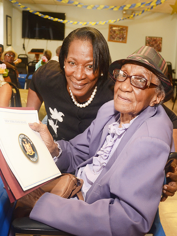 A senior center member smiles holding a certificate of recognition from the New York State Senate.
