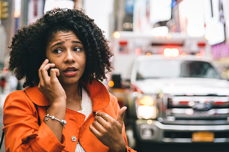 A woman talking outside on her cell phone with an ambulance in the background.
