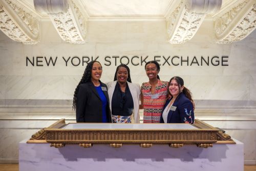 New York City Mayor's Office of Equity Staff stand at the New York Stock Exchange podium. (from left to right) Program Manager Nicole Joseph | Commissioner Sideya Sherman | Deputy Commissioner Dabash Negash | Administrative coordinator Aura Jimenez.