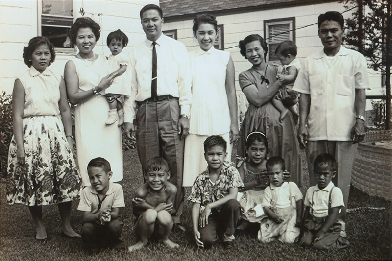 Vintage 1950's photograph of immigrant family of 14 with 4 women in dresses, 2 men wearing suits and 8 children standing in front of a home.