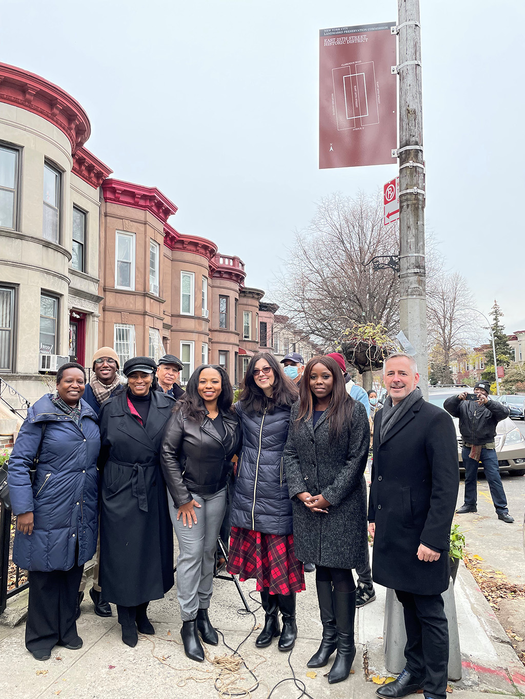 New York City Landmarks Preservation Commission (LPC) Chair Sarah Carroll, New York Landmarks Preservation Foundation (NYLPF) Chair Tom Krizmanic, Council Member Farah Louis and residents of the East 25th Street in East Flatbush pose in front of the historic district marker attatched to a lamp post