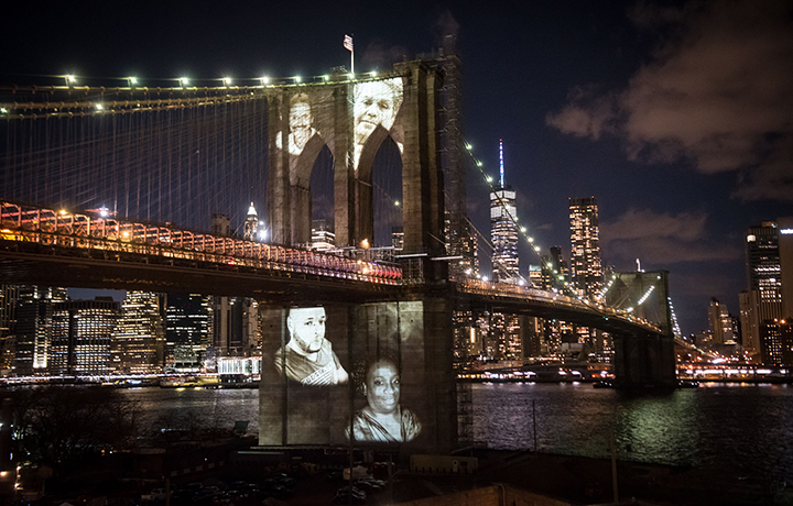 Images of New Yorkers who have passed away due to COVID-19 projected onto the Brooklyn Bridge