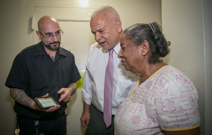 Image of General Manager Michael Kelly with a NYCHA staffmember showing a resident how to work the new digital handheld devices.