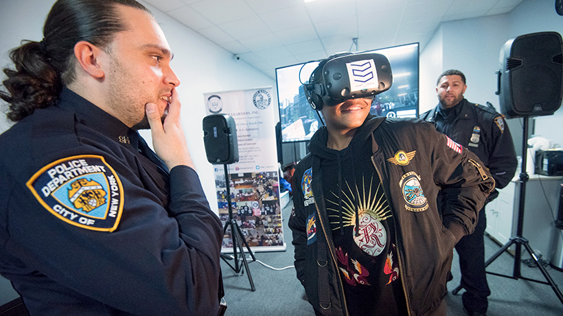 Smiling teenager wearing a VR headset, two amused cops look on.