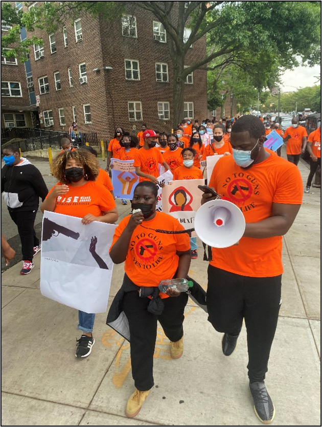 Parade of people in orange t-shirts with signs protesting for Gun Violence Awareness Month