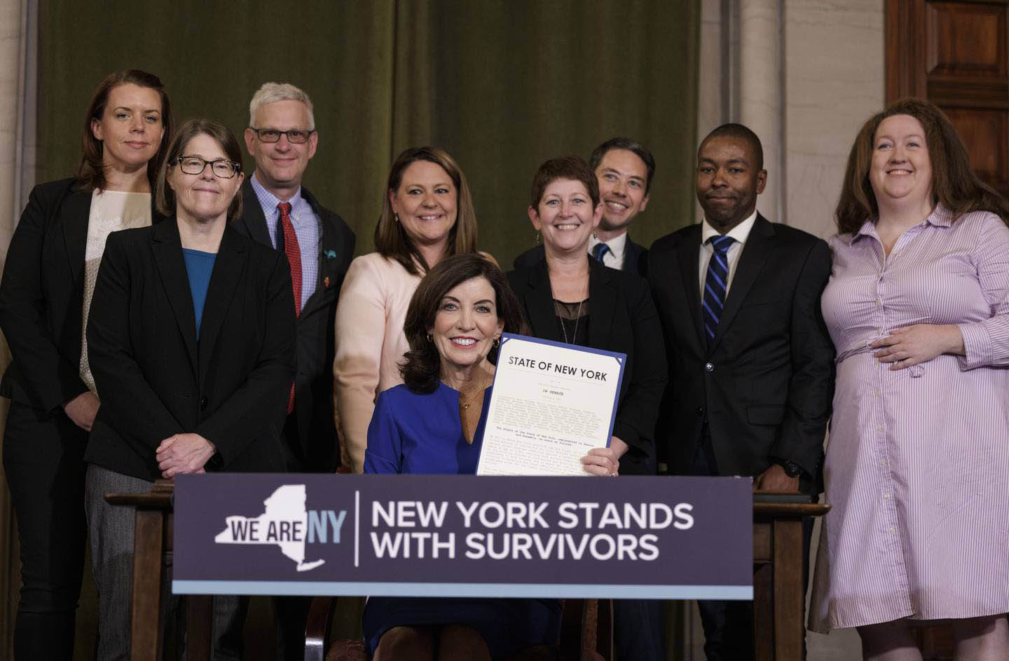 A group of people with NYS State Governor Kathy Holchul posing for a photo at signing of NYS Adult Survivor Act.