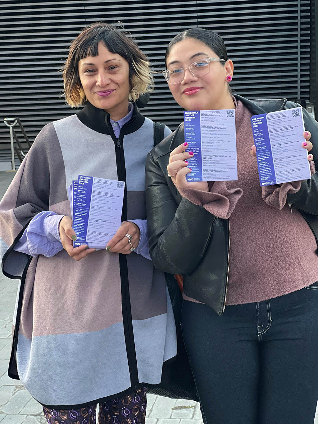 Two woman standing outside in public plaza holding an ENDGBV Go Purple Day Resources Purple Handout Card