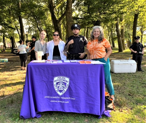 Image of 3 females and NYC Police Officer stationed behind table of flyers and giveaways in Astoria Park Queens