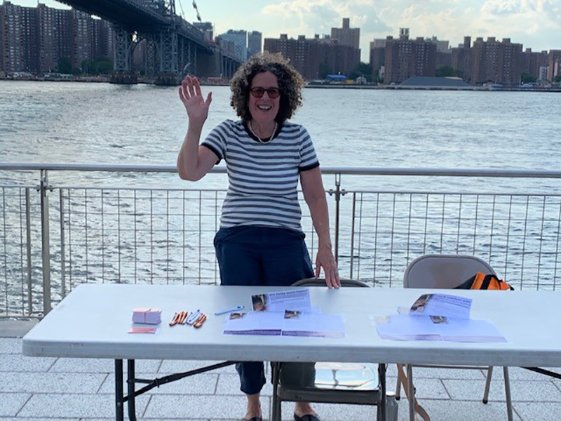 A picture of female on a pier in Brooklyn NY stationed behind table of flyers and giveaways
