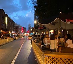 People sitting in outdoor dining spaces along a road.