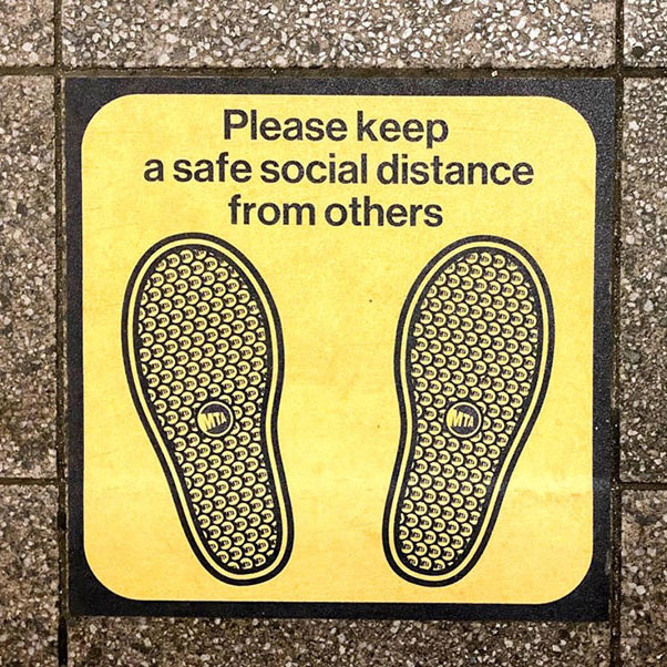 Social distancing marker on the ground with icons of two  feet. Text reads “Please keep a safe social distance from others.”