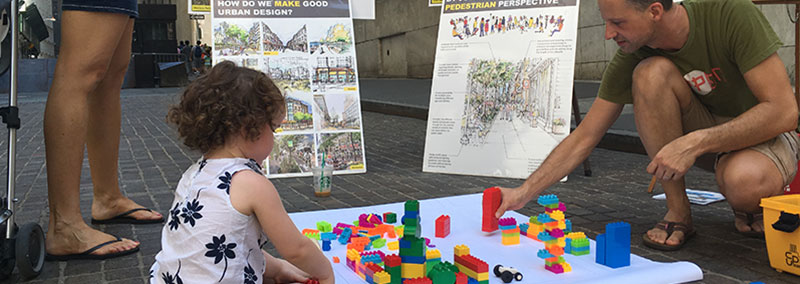Kid and adult playing with legos in front of posters about urban design
