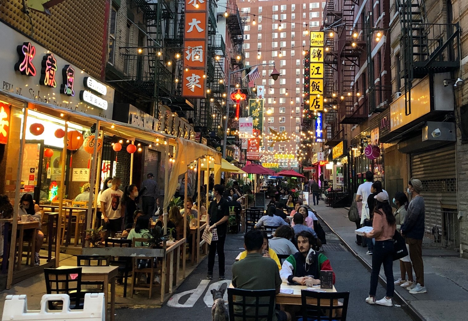 People sitting at tables set up outside businesses on a street in Chinatown that has been closed to traffic
