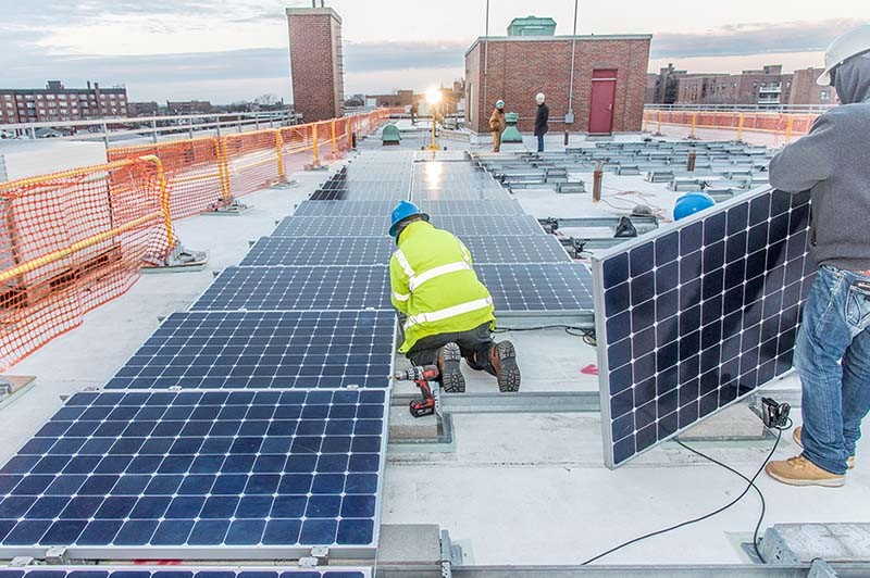 One kneeling worker and one standing worker installing solar panels on a rooftop