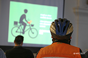 A delivery cyclist wearing a helmet attends a public presentation.