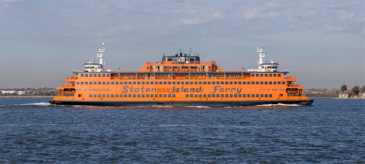 An orange Staten Island Ferry travels in the New York harbor on a sunny day.