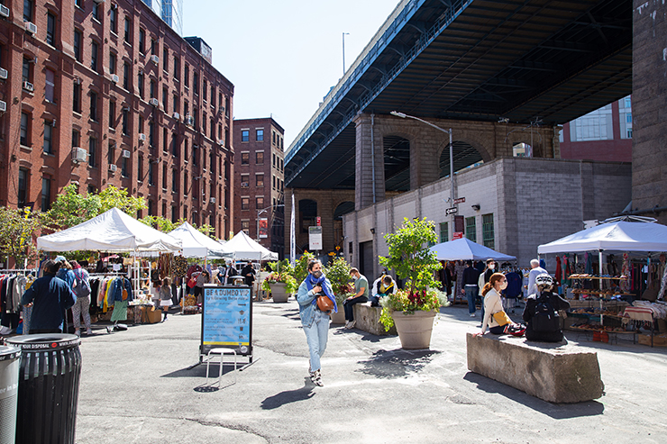 People shopping and sitting outside at Brooklyn Flea Market in DUMBO Plaza, Brooklyn, NY.
